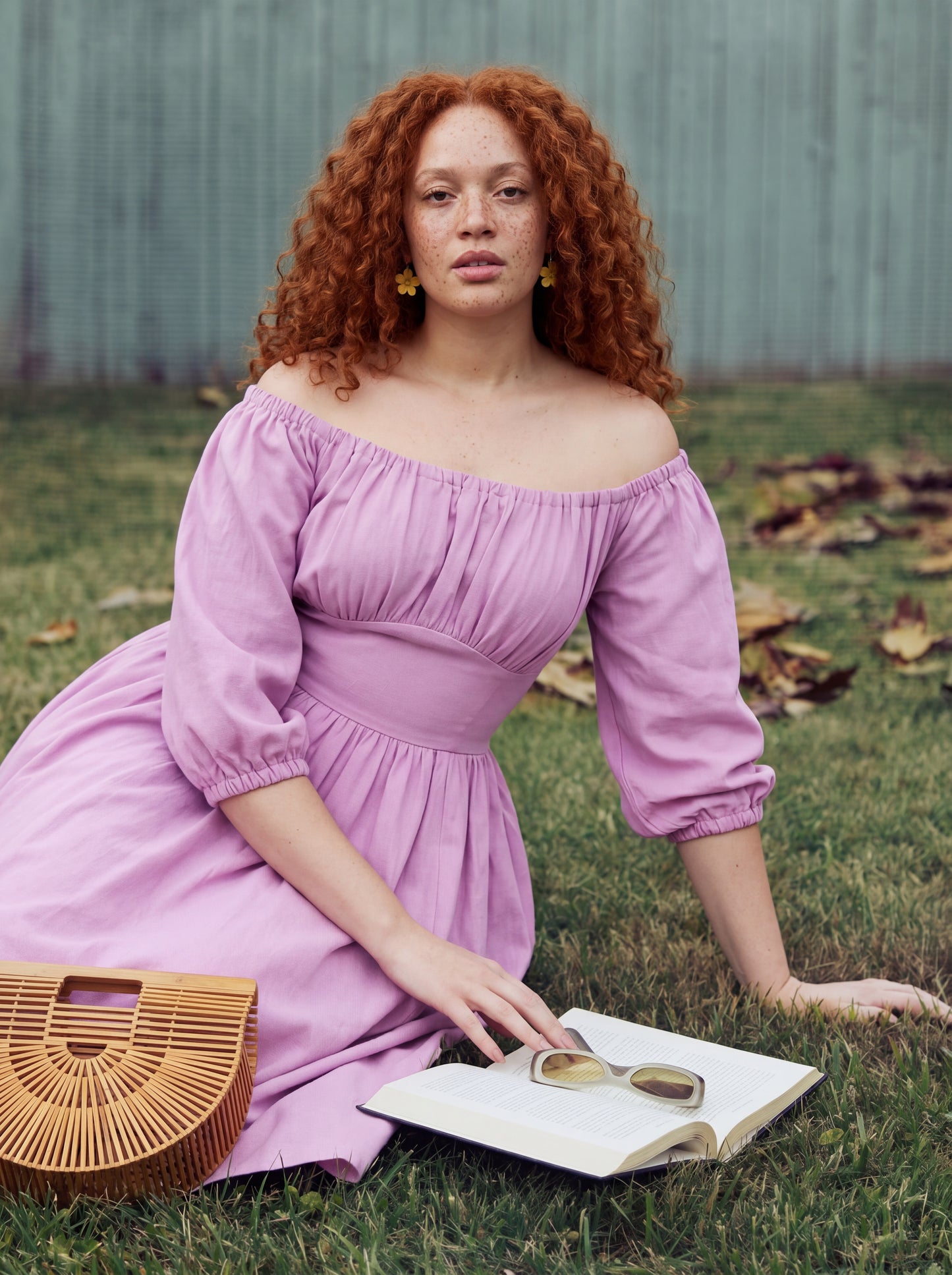 Marie-Therese peasant dress in Pinup Girl pink, seated on grass with a book, showing the off-shoulder neckline and gathered waist