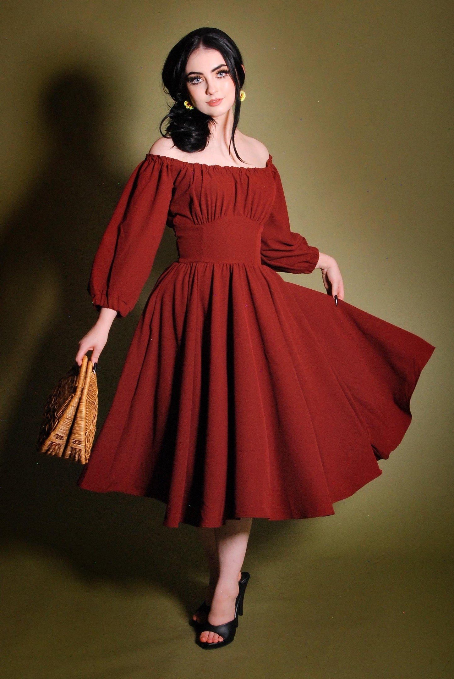 Model in the Marie-Therese merlot peasant dress, a deep wine-red 70s day dress worn off the shoulder with long blouson sleeves, a fitted waistband and a full twirl skirt with pockets