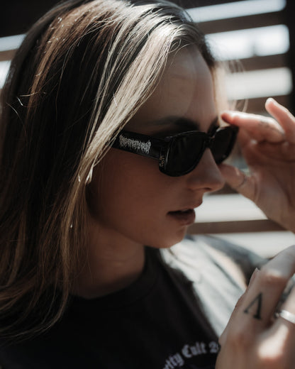 Model wearing the Black Metal sunglasses in shiny black with a logo across the temple, by The Pretty Cult