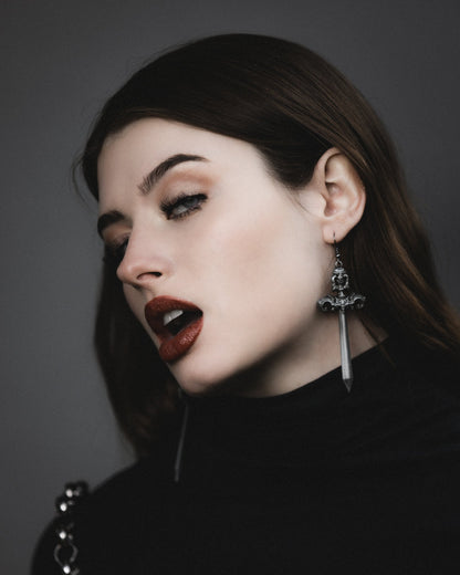 Woe Blade silver sword earrings worn with a black turtleneck, The Pretty Cult