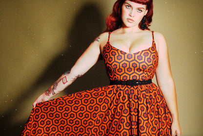 Model in the Amalie swing dress in orange and black Hotel Hexagon print, belted at the waist, showing the fitted ballerina bodice and full gathered skirt