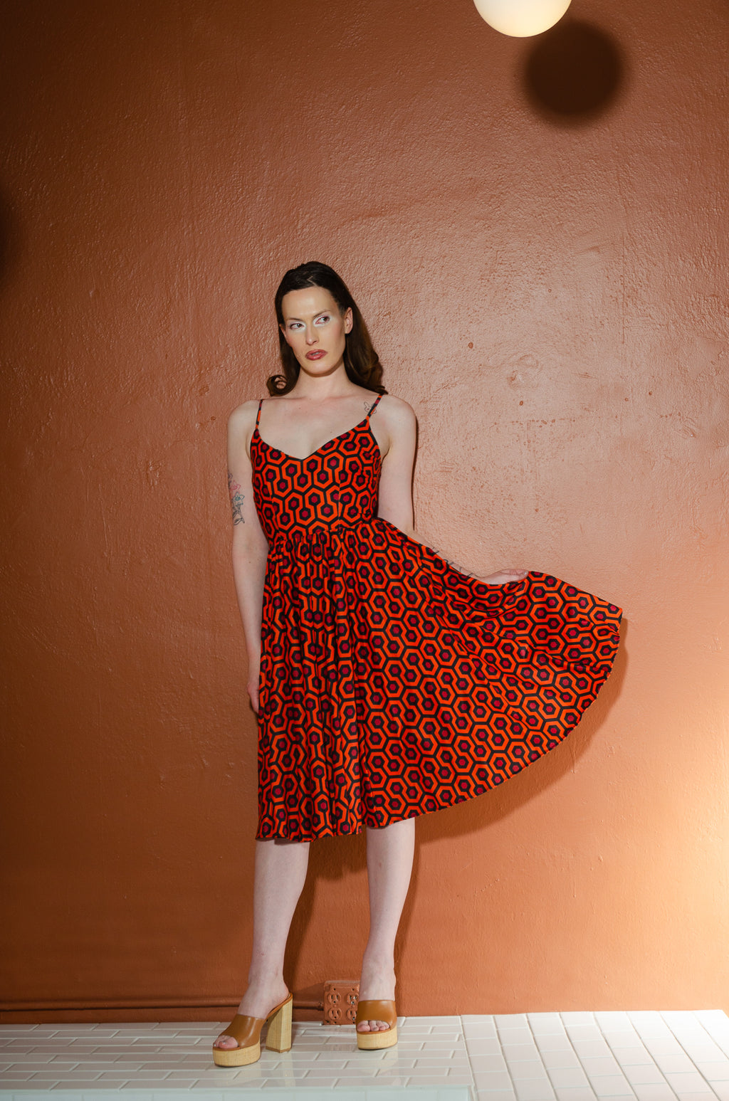 Model lifting the skirt of the Amalie Hotel Hexagon swing dress to show its full sweep and adjustable spaghetti straps