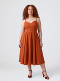 Model wearing the Amalie Ballerina 70s swing dress in Amber Harvest, a deep spiced orange with a fitted bodice and full gathered skirt to mid-calf