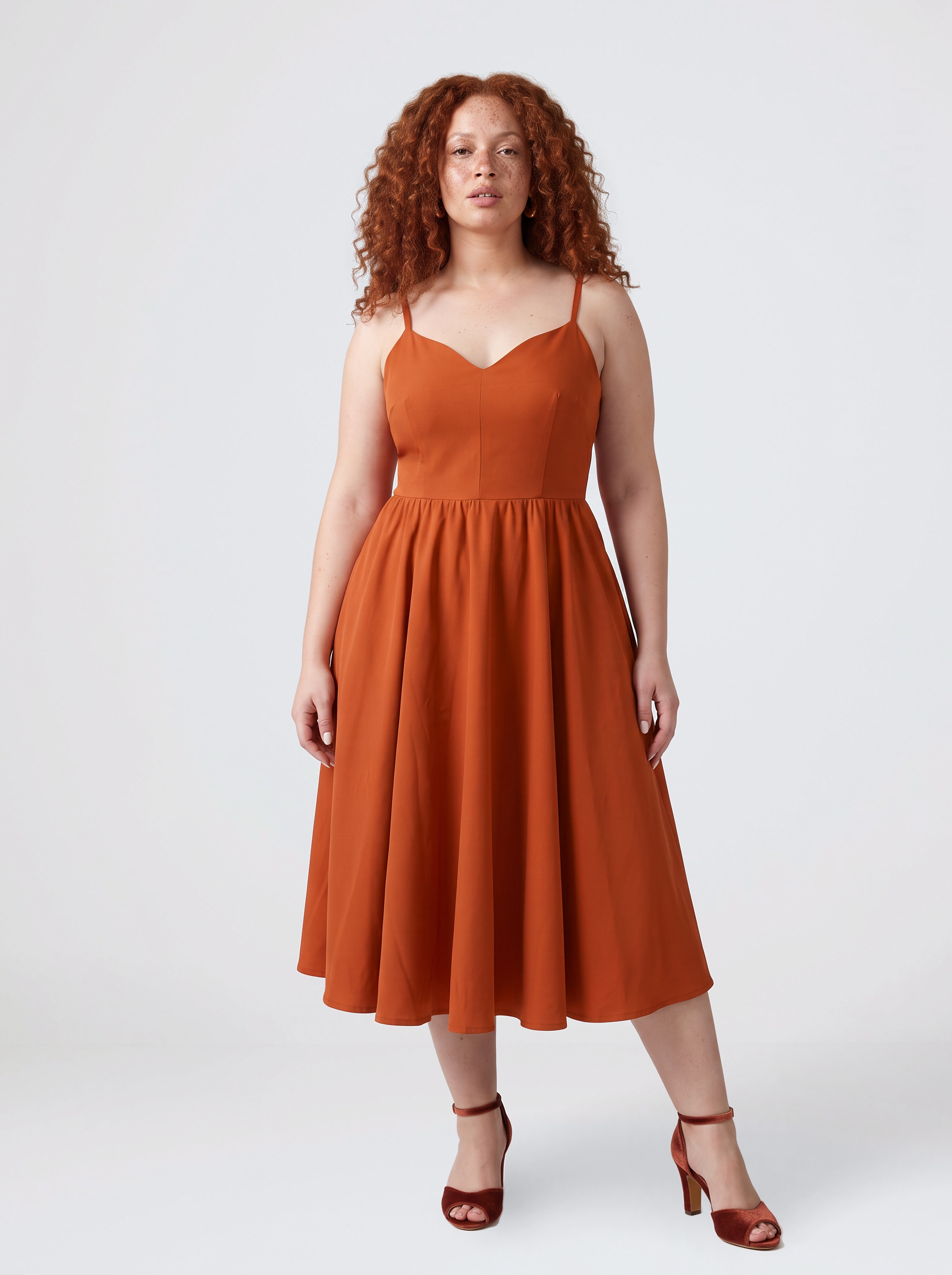 Model wearing the Amalie Ballerina 70s swing dress in Amber Harvest, a deep spiced orange with a fitted bodice and full gathered skirt to mid-calf
