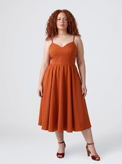 Model wearing the Amalie Ballerina 70s swing dress in Amber Harvest, a deep spiced orange with a fitted bodice and full gathered skirt to mid-calf