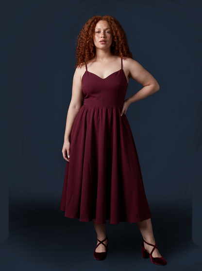 Burgundy Amalie swing dress against a dark backdrop, one hand on the hip, showing the sweetheart neckline and full skirt