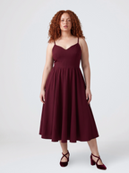 Model wearing the Amalie Ballerina 70s swing dress in burgundy, fitted bodice with spaghetti straps and a full gathered skirt to mid-calf