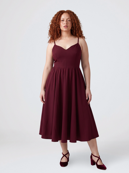 Model wearing the Amalie Ballerina 70s swing dress in burgundy, fitted bodice with spaghetti straps and a full gathered skirt to mid-calf