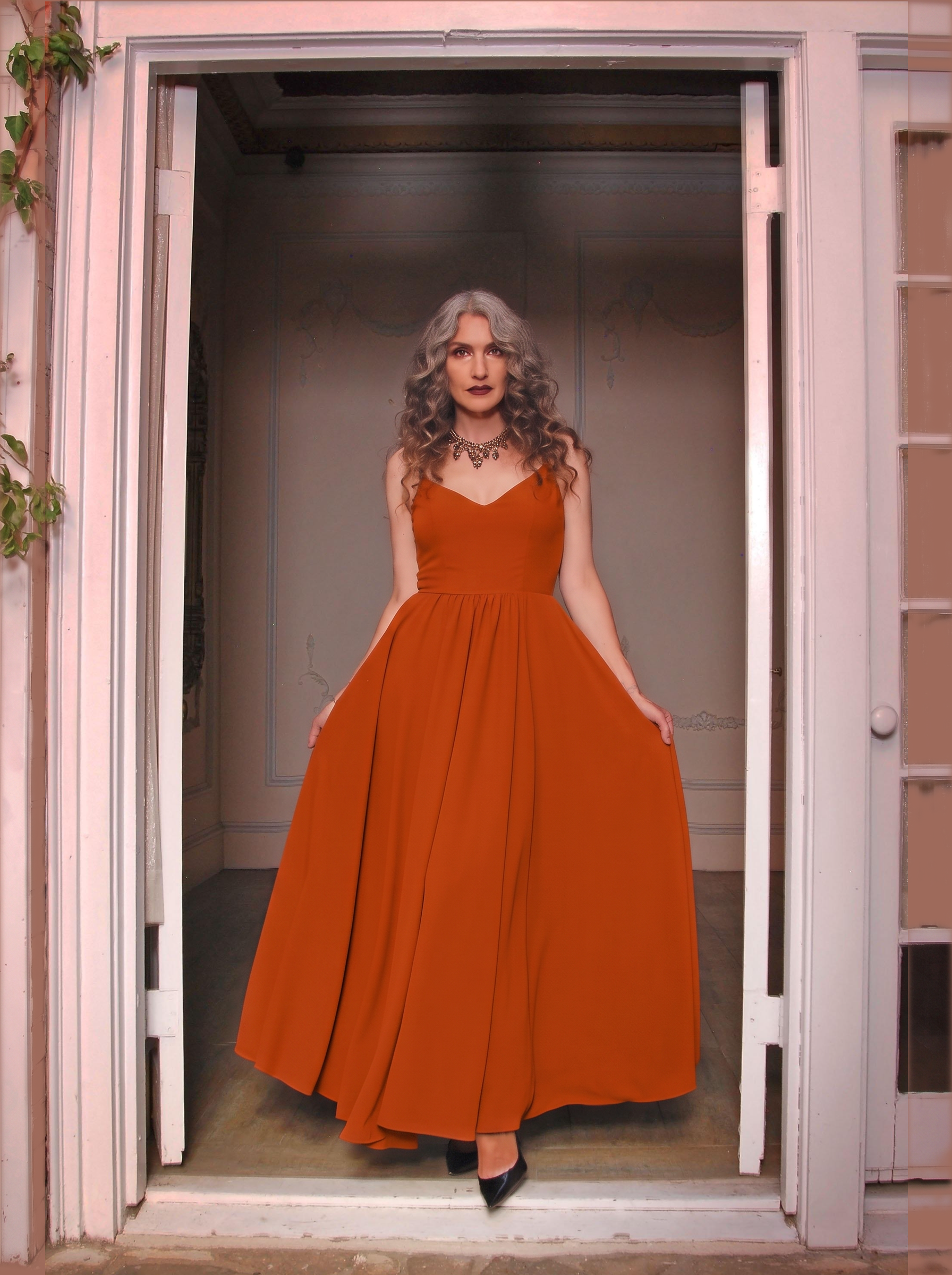 Amber Harvest Amalie maxi gown worn in a doorway, spiced orange skirt falling to the floor