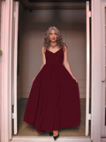 Burgundy Amalie maxi gown worn in a doorway, floor-length skirt falling to black heels