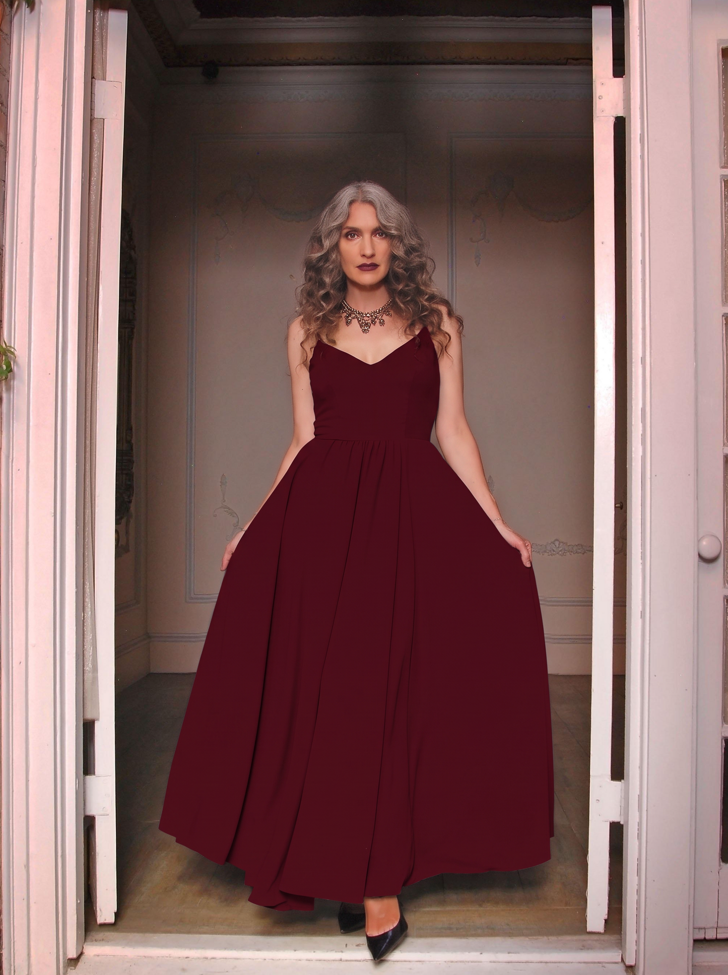 Burgundy Amalie maxi gown worn in a doorway, floor-length skirt falling to black heels