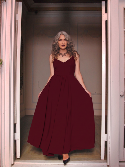Burgundy Amalie maxi gown worn in a doorway, floor-length skirt falling to black heels