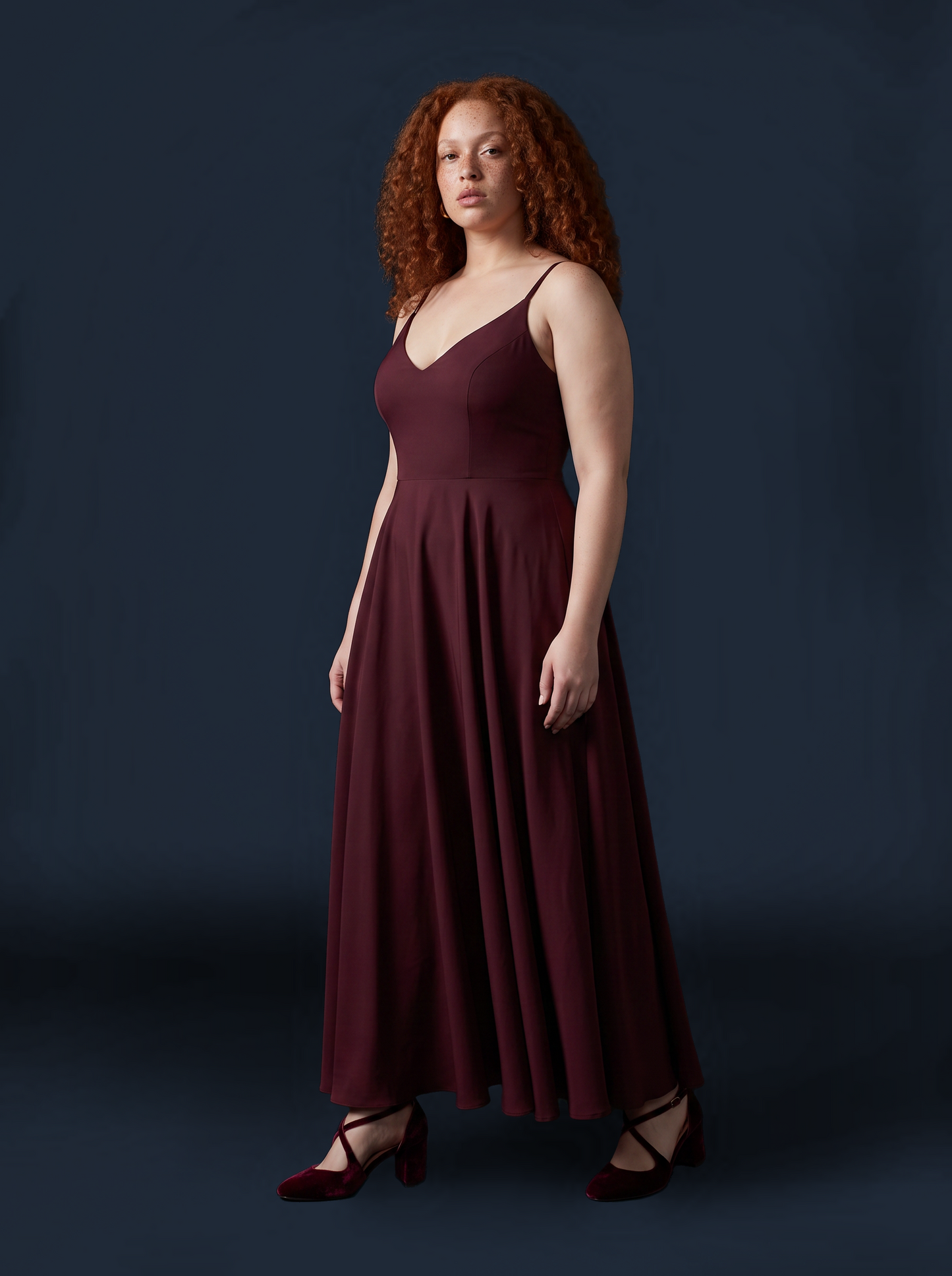 Burgundy Amalie maxi gown photographed against a dark backdrop, three-quarter view showing the full sweep of the gathered skirt