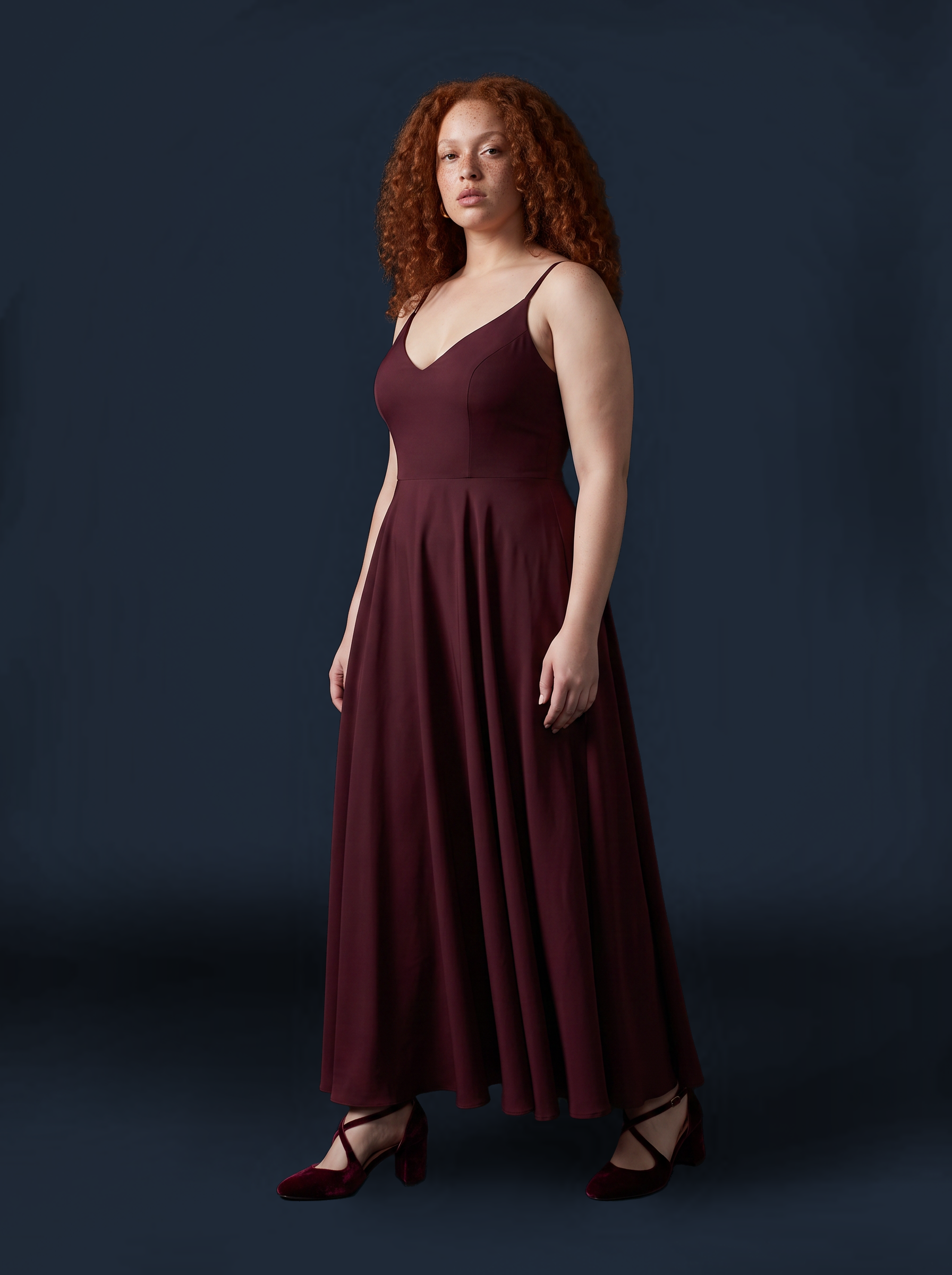 Burgundy Amalie maxi gown photographed against a dark backdrop, three-quarter view showing the full sweep of the gathered skirt