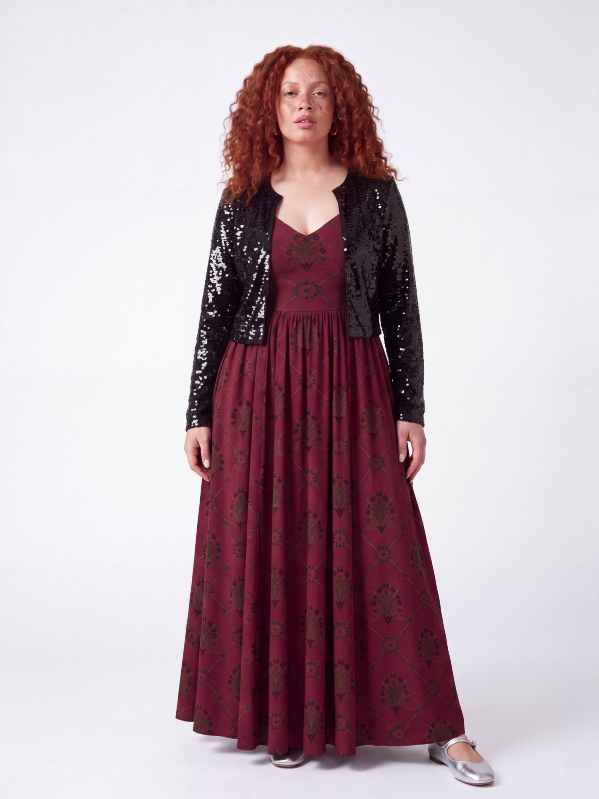 Model wearing the Amalie Ballerina Daytime Maxi Gown in Goth Grand Trianon under a cropped black sequin jacket, a fall evening look with the fitted bodice and burgundy and black print showing