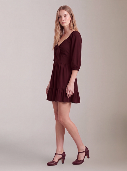Molly Mini dress in burgundy, three-quarter side view, showing the flared tiered skirt and elbow-length puff sleeves.