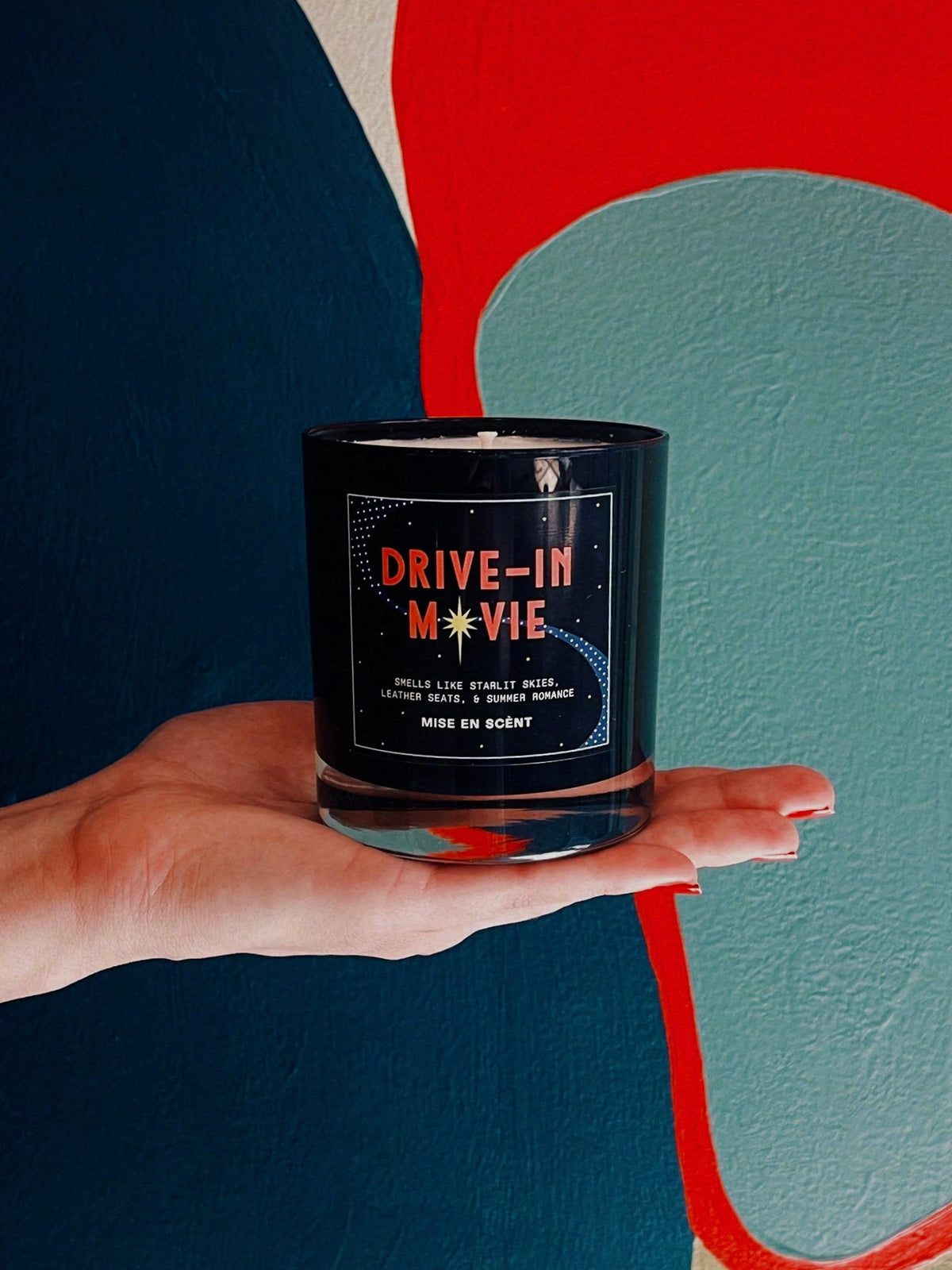 Drive-In Movie candle held in hand against a colorful mural