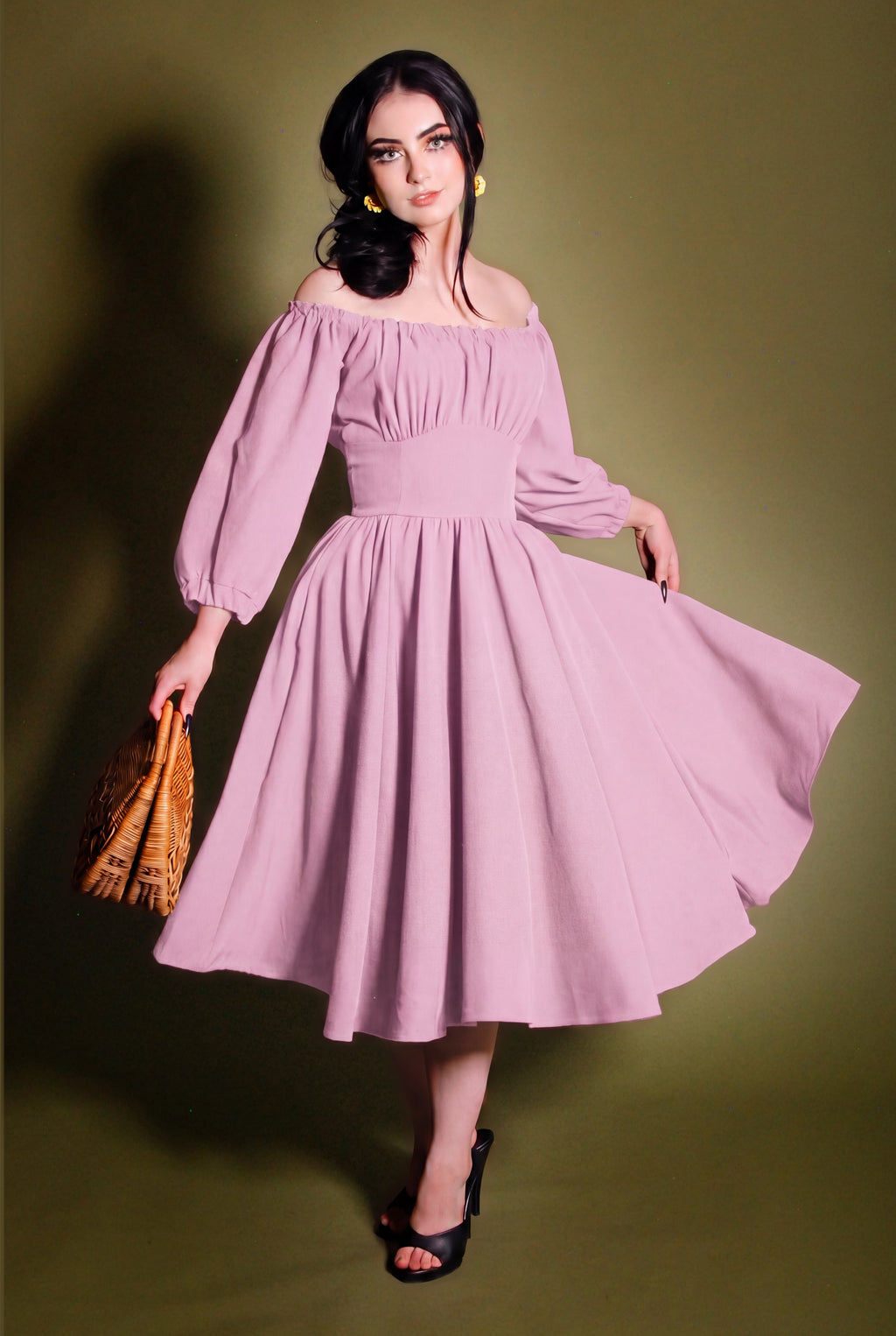 Marie-Therese peasant dress in Pinup Girl pink, off-shoulder bodice and full midi skirt, worn with a tan bag on a dark backdrop