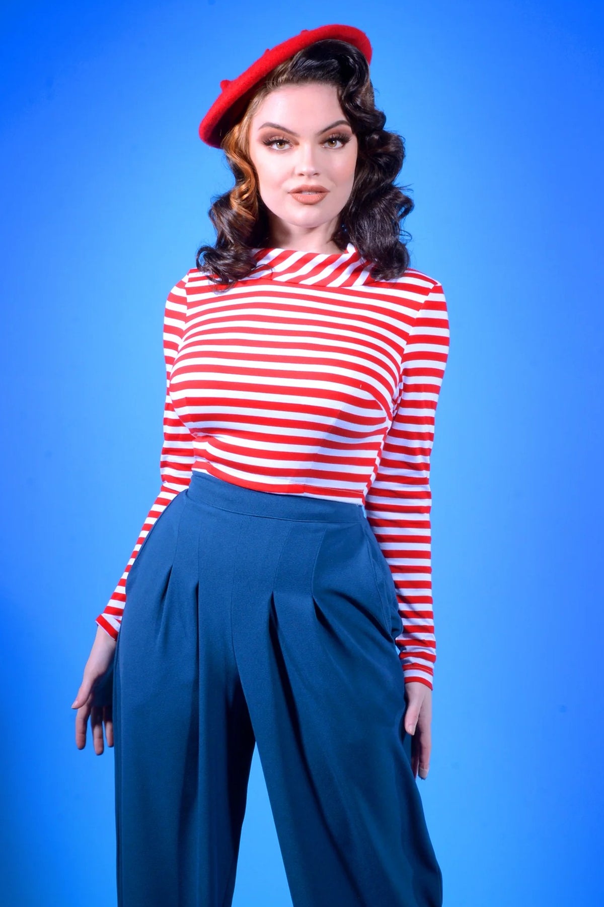 Model wearing the Joanna long sleeve crop top in red and white striped knit with high-waisted navy pleated trousers and a red beret, framed head to thigh