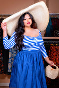 Model wearing the Kayla top in blue and white stripe knit with 3/4 sleeves and gathers at the bust, a royal blue full skirt and an oversized straw sun hat
