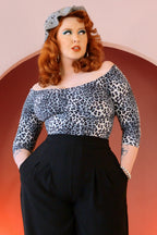 Model wearing the Kayla top in grey leopard crepe off the shoulder with 3/4 sleeves, tucked into black high-waisted wide-leg trousers, hands in pockets