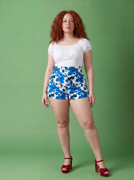 LB high-waisted shorts in Fiori Dolce Blue, a blue and white painted floral cotton sateen, worn with a white peasant top, by Pinup Girl Clothing, sizes XS to 5X