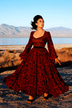 Model twirling in the Lucrezia renaissance maxi gown in black on red Capri Floral, the full circle skirt swinging out, bishop sleeves and a slim black belt at the waist