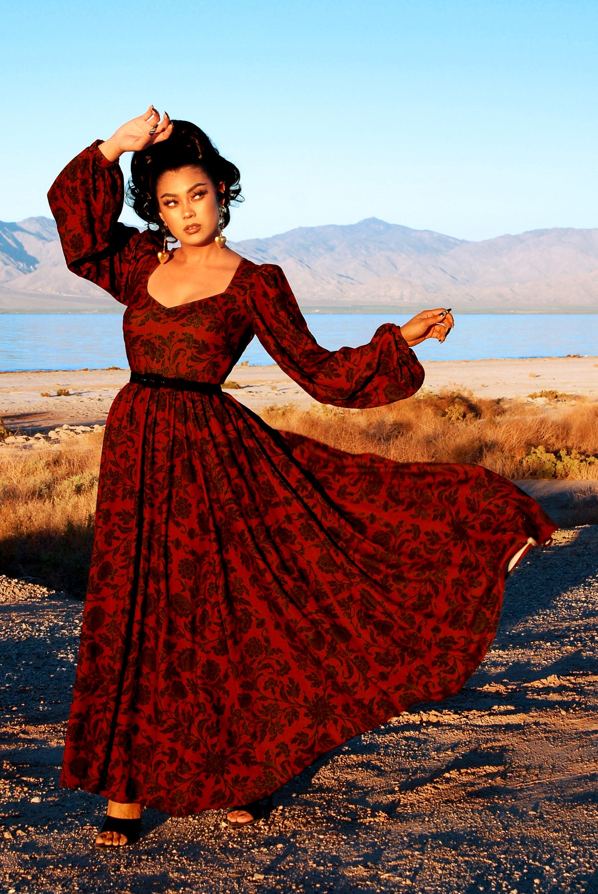 Lucrezia renaissance maxi gown in black on red Capri Floral with one arm raised to show the full bishop sleeve gathered at the cuff and the deep sweetheart neckline