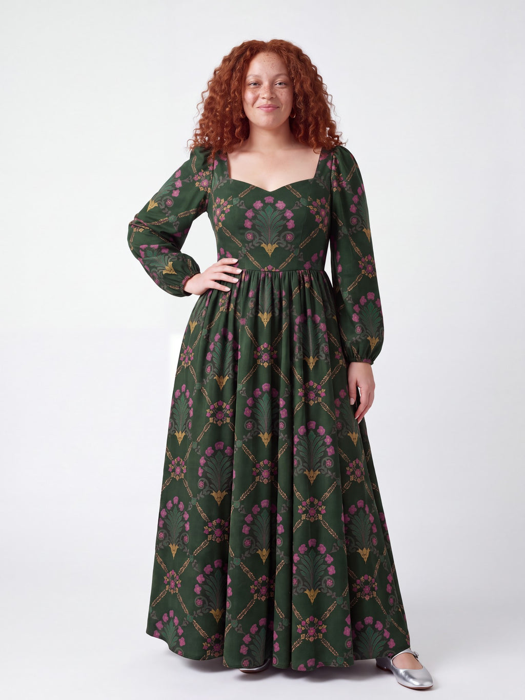 Model smiling in the Lucrezia Renaissance Maxi Gown in Dark Green Grand Trianon, one hand on her hip, the gathered circle skirt grazing the floor