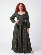 Model smiling in the Lucrezia Renaissance Maxi Gown in Dark Green Grand Trianon, one hand on her hip, the gathered circle skirt grazing the floor