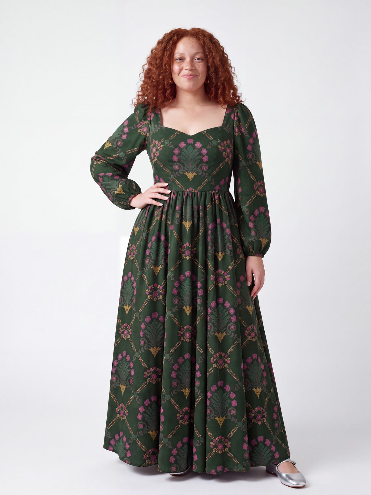 Model smiling in the Lucrezia Renaissance Maxi Gown in Dark Green Grand Trianon, one hand on her hip, the gathered circle skirt grazing the floor