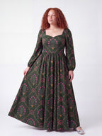 Model in the Lucrezia Renaissance Maxi Gown in Dark Green Grand Trianon, gazing off to the side and holding out the full circle skirt to show the green, pink and gold print