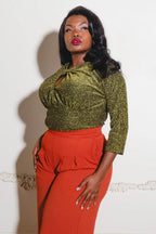 Model wearing the Malia top in sparkly gold lurex ponte with its keyhole neckline and 3/4 sleeves, tucked into high-waisted rust trousers