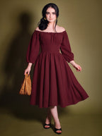 Model in the Marie-Therese burgundy peasant dress, a deep wine-red 70s day dress worn off the shoulder with long blouson sleeves, a wide fitted waistband and a full midi skirt with pockets