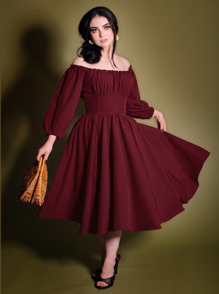 Marie-Therese burgundy peasant dress with the full skirt swept out to one side, showing the gathered off-shoulder neckline, long blouson sleeves and fitted waistband