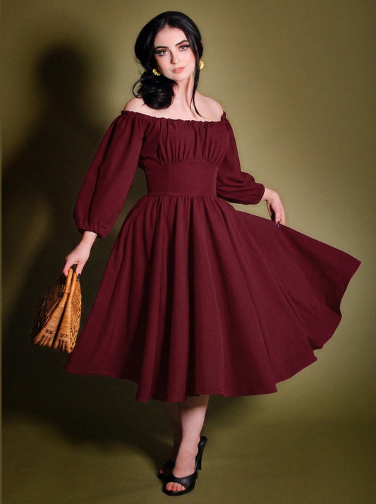 Marie-Therese burgundy peasant dress with the full skirt swept out to one side, showing the gathered off-shoulder neckline, long blouson sleeves and fitted waistband