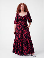 Model in the Molly 70s Maxi Gown in Black and Red Ambrosia Floral, front view, red roses on a black ground with 3/4 puff sleeves and a tiered skirt