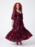 Model laughing and twirling in the Molly 70s Maxi Gown in Black and Red Ambrosia Floral, the tiered skirt flaring out