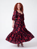 Model laughing and twirling in the Molly 70s Maxi Gown in Black and Red Ambrosia Floral, the tiered skirt flaring out