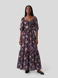 Model in the Molly 70s Maxi Gown in Oil Slick Ambrosia Floral, front view, small lilac and plum roses on dark olive green crepe with 3/4 puff sleeves and an ankle-length tiered skirt over black flats