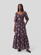 Model with one hand in the deep side pocket of the Molly 70s Maxi Gown in Oil Slick Ambrosia Floral, showing the tie-front sweetheart neckline and gathered bodice