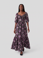 Model walking in the Molly 70s Maxi Gown in Oil Slick Ambrosia Floral, the tiered skirt swaying above black ballet flats