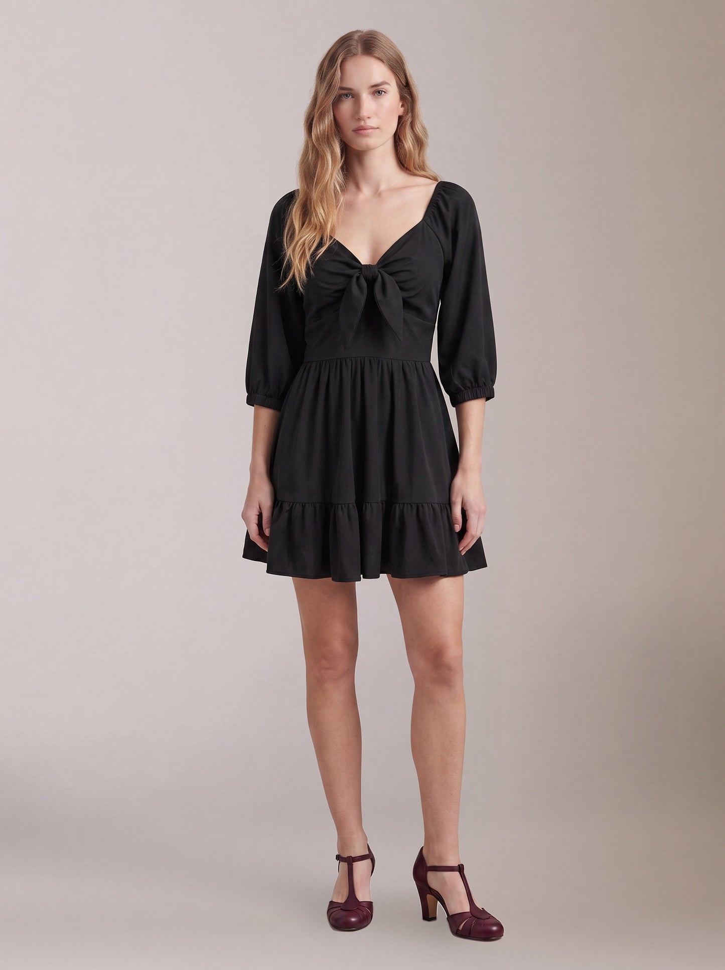 Model wearing the Molly Mini dress in solid black, front view, with tie-front bodice and tiered ruffle hem skirt.