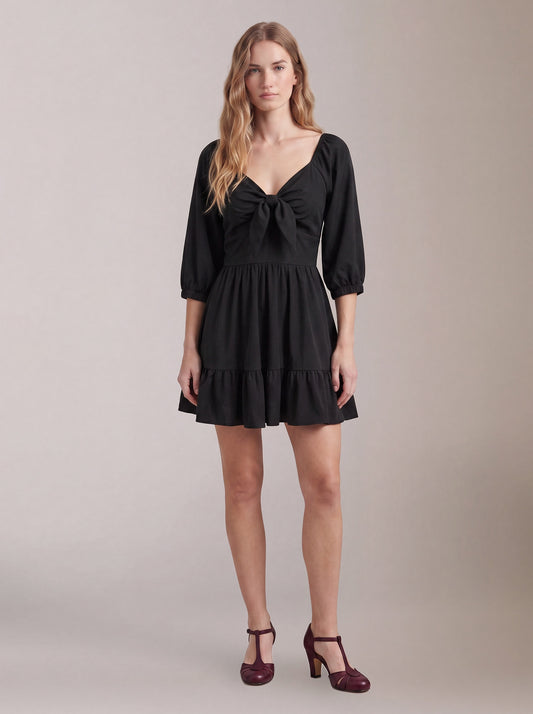 Model wearing the Molly Mini dress in solid black, front view, with tie-front bodice and tiered ruffle hem skirt.