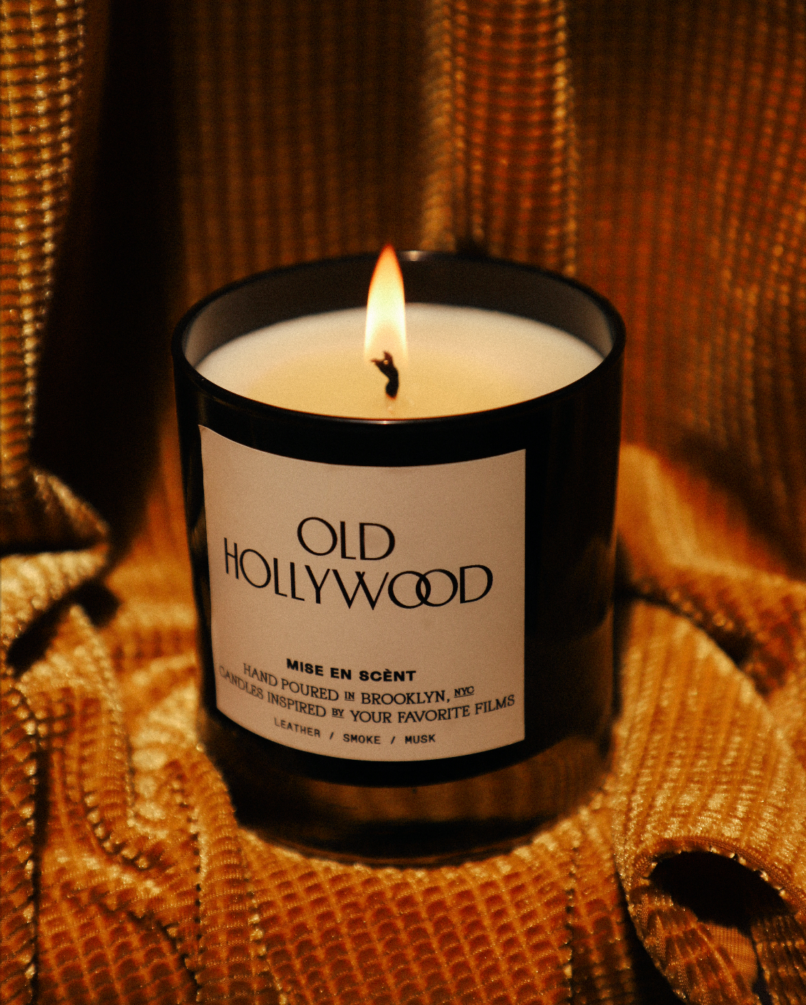 Old Hollywood candle lit on gold fabric