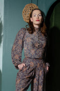 Model wearing the Serafina top in the grey Royal Woods print with a high buttoned collar and bishop sleeves, hands in the pockets of matching print trousers
