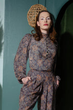 Model wearing the Serafina top in the grey Royal Woods print with a high buttoned collar and bishop sleeves, hands in the pockets of matching print trousers