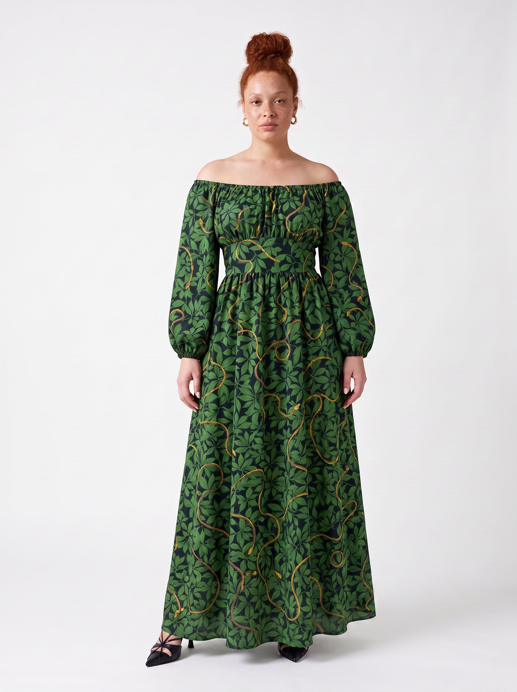 Model wearing the Swann Maxi Dress in Black Serpente, green foliage and gold snakes on black, off the shoulder with long blouson sleeves, floor length