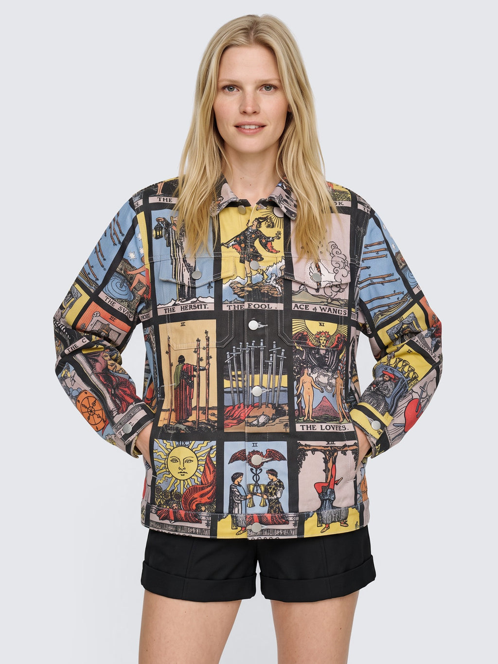 Model with both hands in the pockets of the oversized Tarot Card Denim Jacket, buttoned, worn with black high-waisted shorts