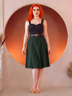 Front view of the Viva 40s Tulip Skirt in Hunter Green with the black Varla Top, the paneled skirt flaring from a belted waist to just below the knee, worn with tan bow sandals